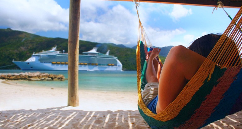 Cruise ship in island port in the background with a woman in a hammock in the foreground