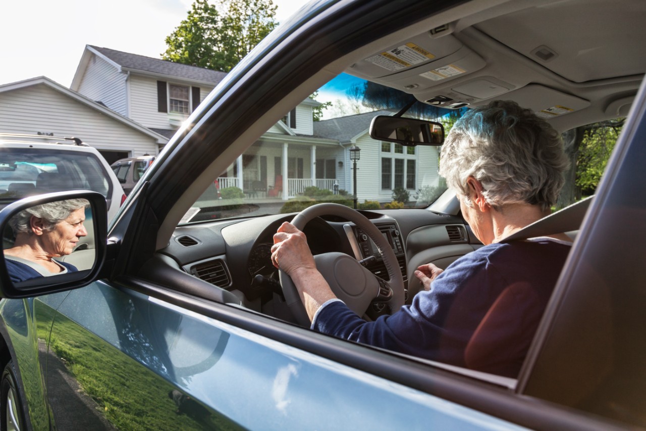 An authentic real person, real life senior adult woman driver wearing her seat belt is adjusting and becoming acquainted with the dashboard controls and features of her brand new car while parked in her driveway before she drives it on the road for the first time.
