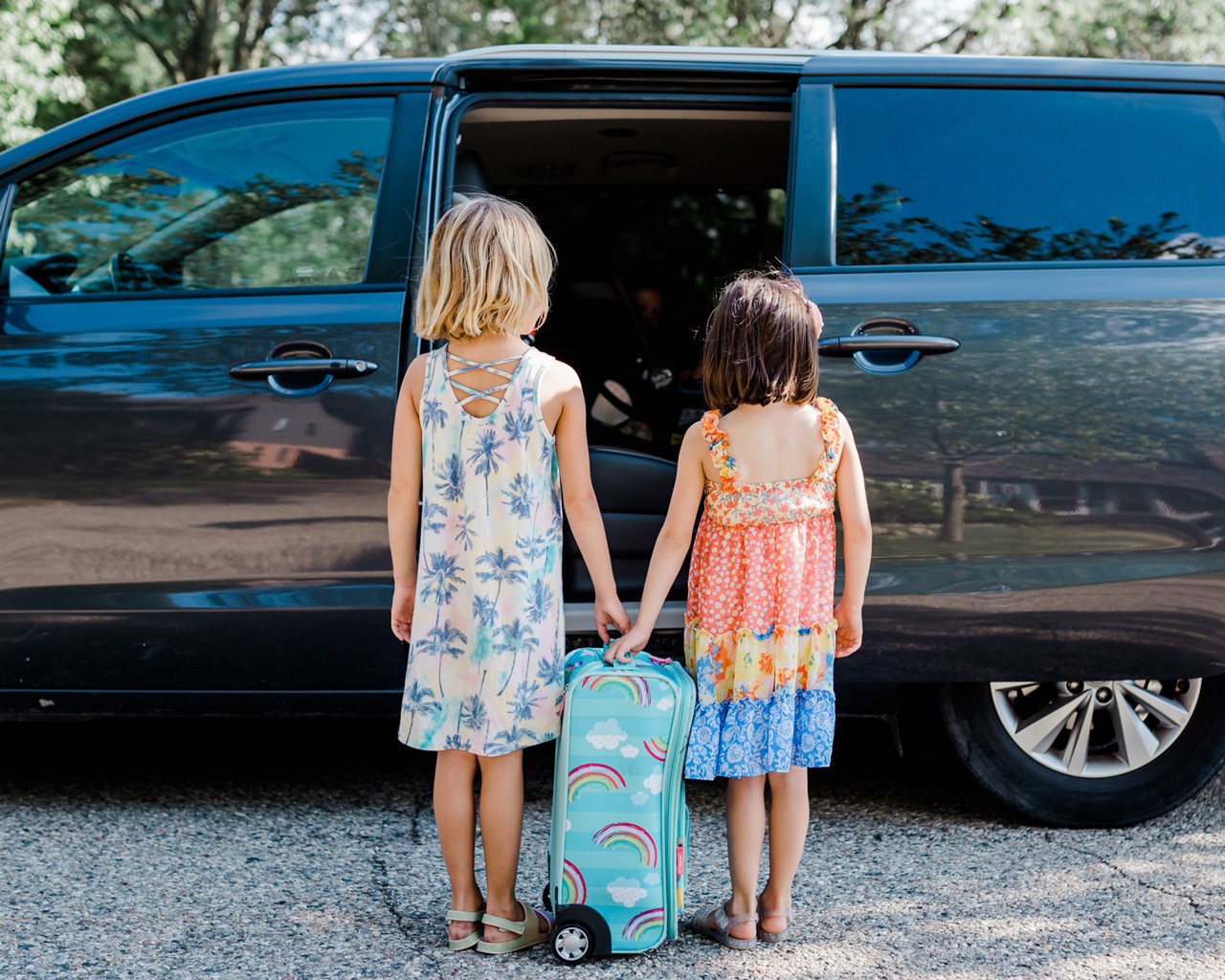 Two girls with suitcase getting in a mini van for a road trip.