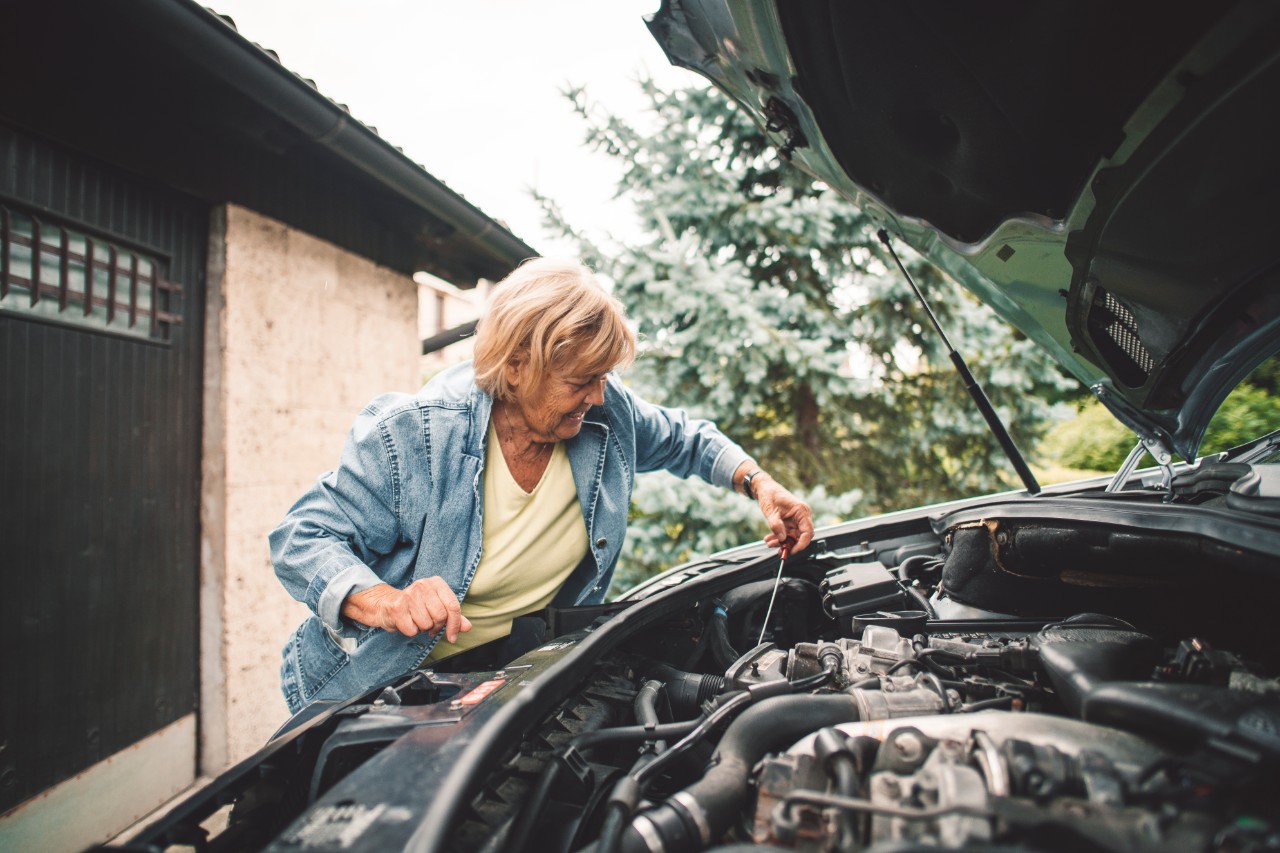 Woman trying to repair a broken down car. Checking oil level in car engine, open car hood, worried looking at car engine.