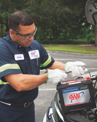 A person changing their car battery with a battery that has a AAA logo on it.