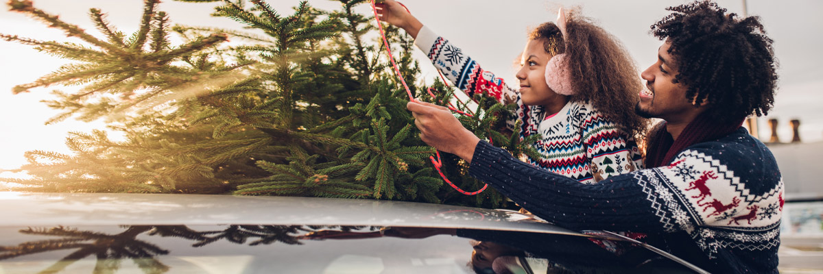 family putting with christmas tree on top of car  