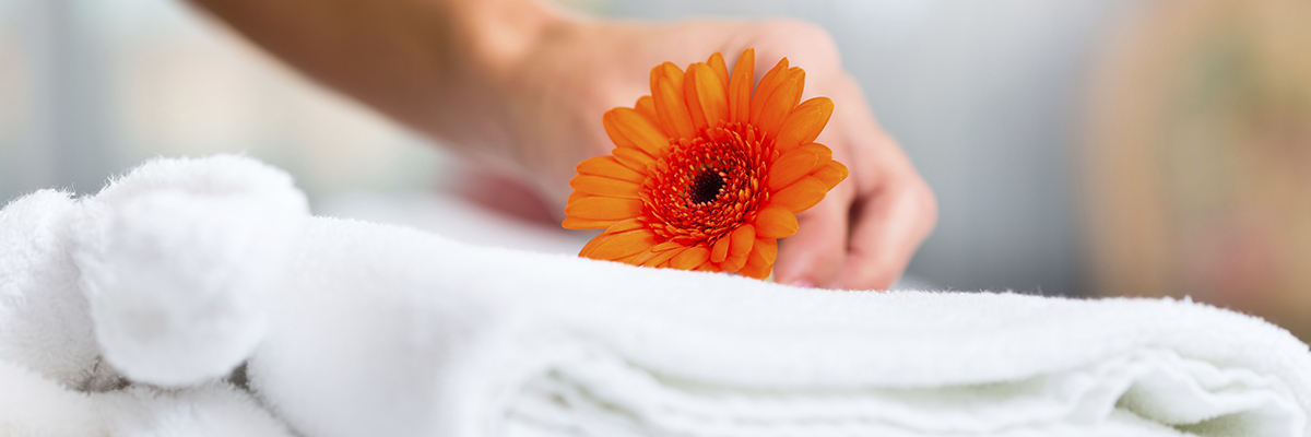 fresh orange daisy being placed on fresh towels linens in a AAA approved hotel